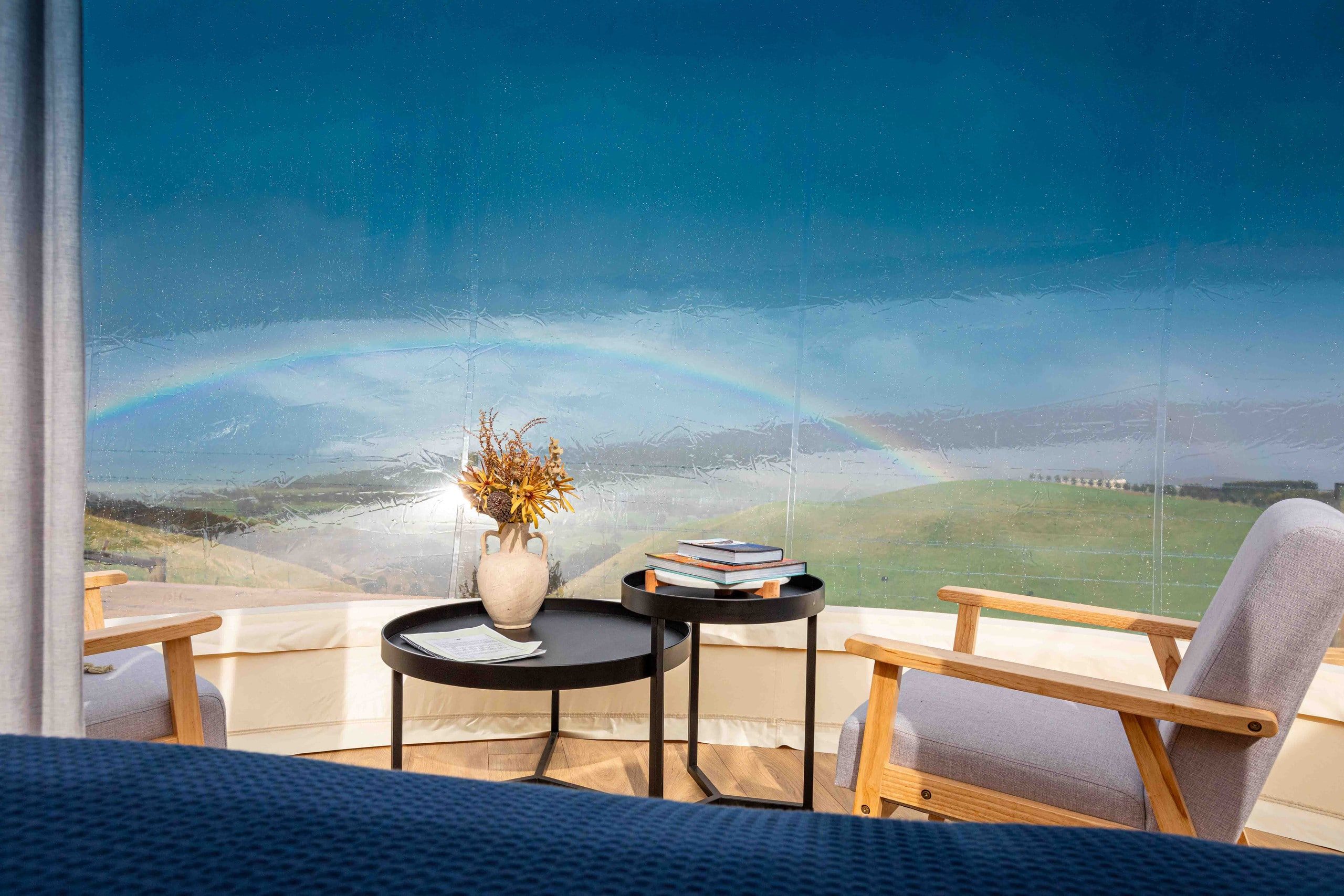 Inside the bubble — armchairs facing a rainbow over the green hills